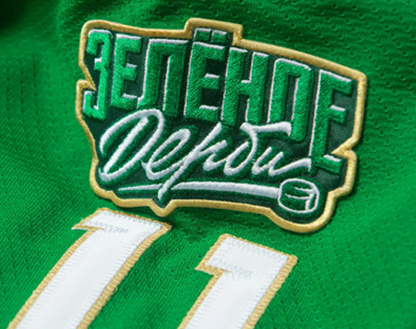 Изображение зелёной хоккейной формы с вышитыми словами Зелёное дерби и цифрами 11 внизу. Текст выполнен в бело-золотых цветах, рядом изображён маленький хоккейный шайба